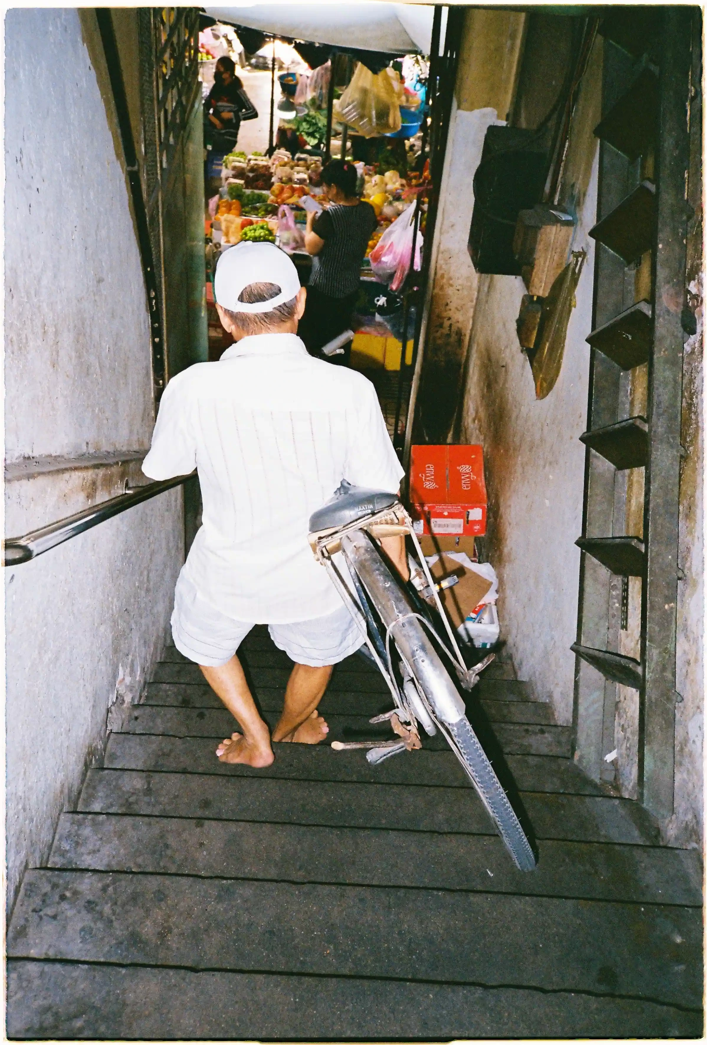 Ảnh chụp trong điều kiện thiếu sáng bằng Nikon L35AF, flash làm sáng rõ một người đàn ông và chiếc xe đạp trên cầu thang, bắt trọn khoảnh khắc di chuyển - Fuji 400.