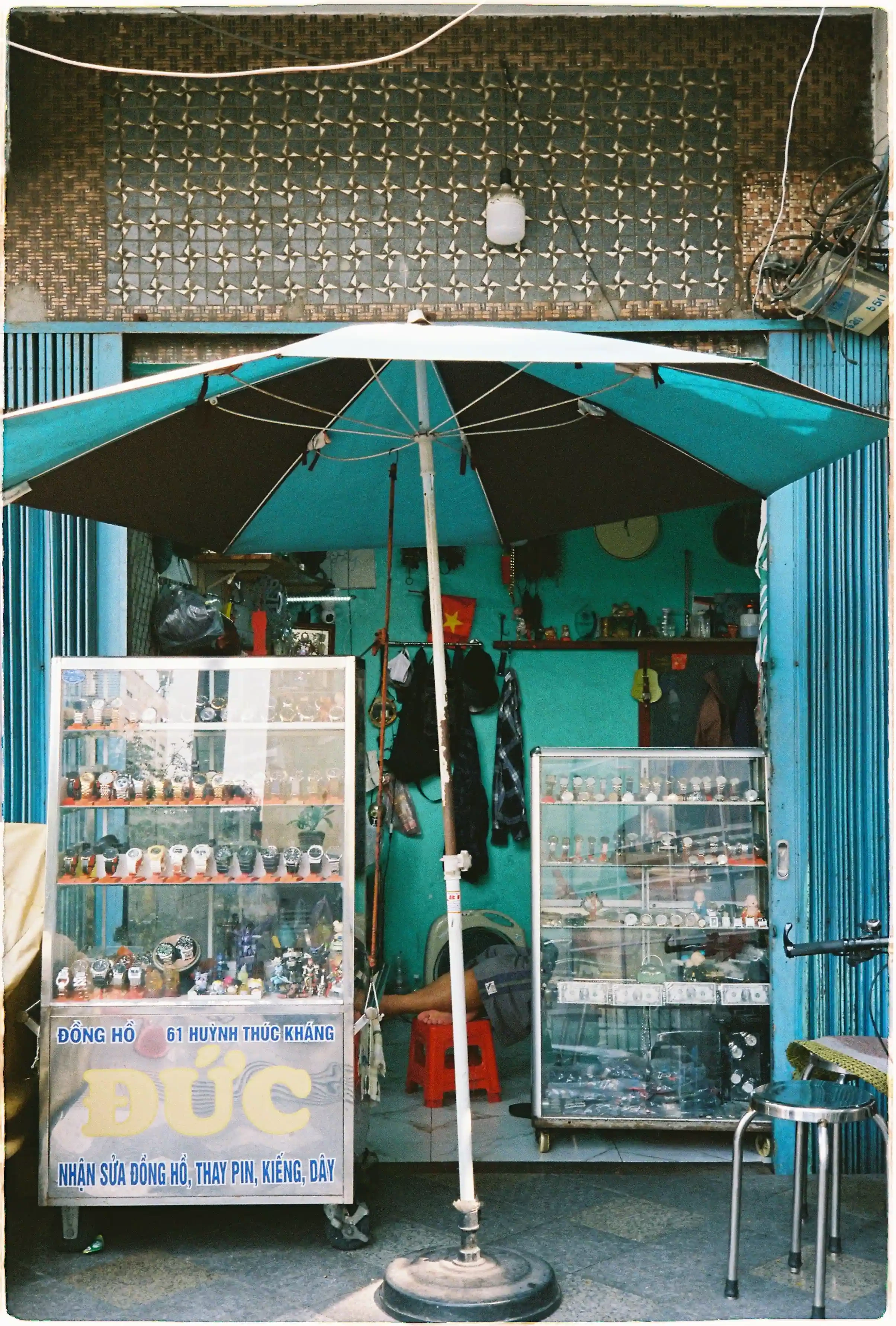 Ảnh chụp tiệm sửa đồng hồ đường phố bằng Rollei 35 SE, tái tạo màu xanh đặc trưng của cửa sắt và tường vôi, chi tiết sắc nét qua tủ kính. Rollei 35 SE, f/11, 1/125s, Fuji 400