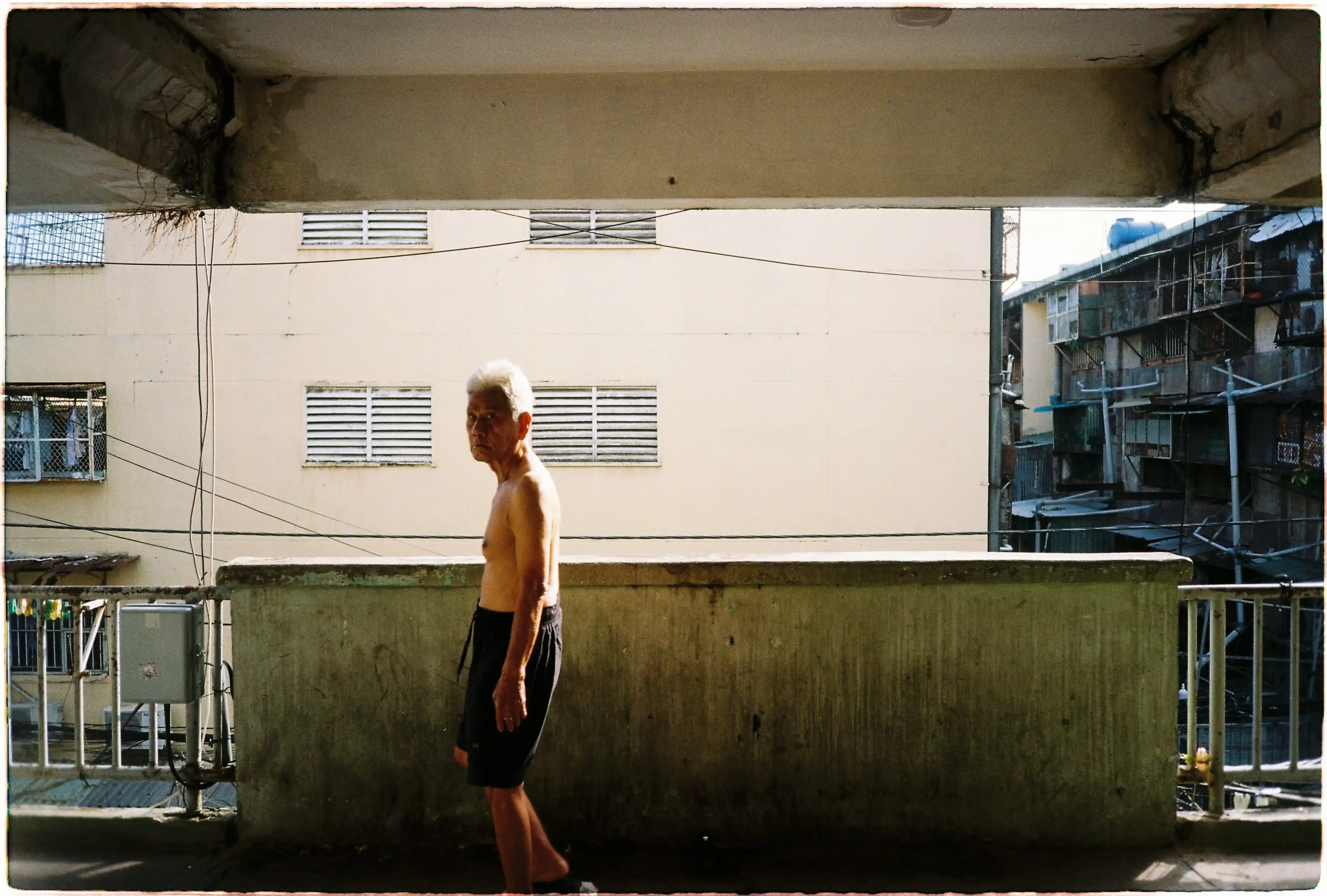 Ảnh chụp ông cụ đứng ở hành lang chung cư bằng Fuji Tiara 1 chế độ Tắt Flash: Đo sáng chuẩn xác vào chủ thể trong điều kiện ngược sáng nền - Kodak Gold 200