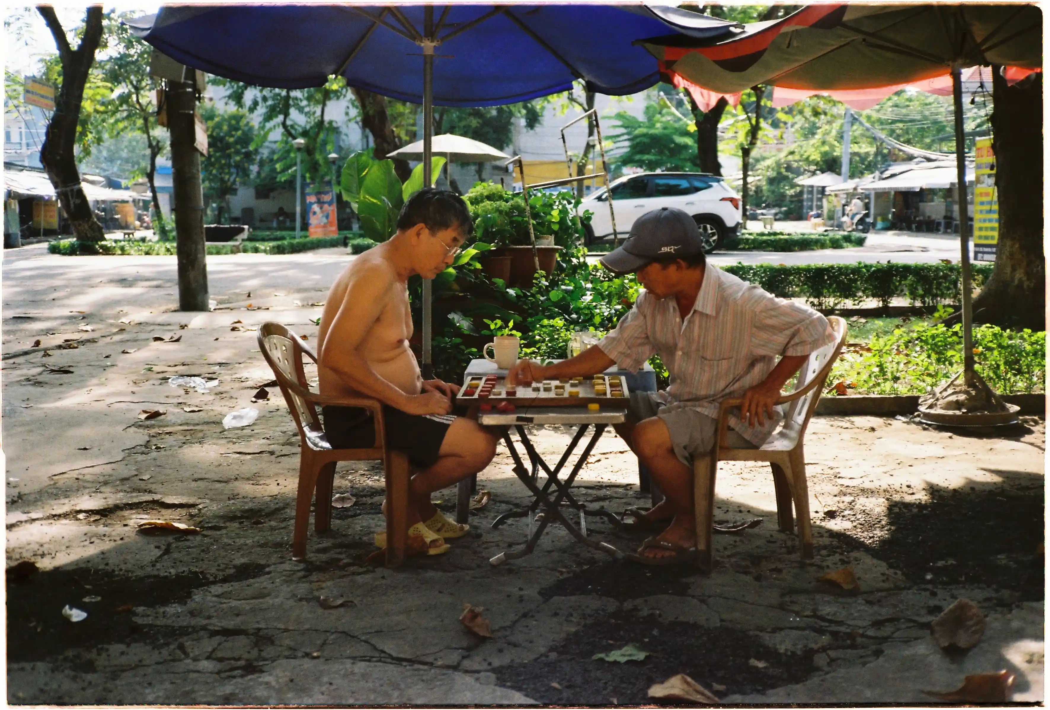 Hai người đàn ông chơi cờ tướng dưới dù: Canon Autoboy 3 xử lý tốt tình huống ngược sáng nhẹ, giữ chi tiết chủ thể trong bóng râm - Kodak Gold 200