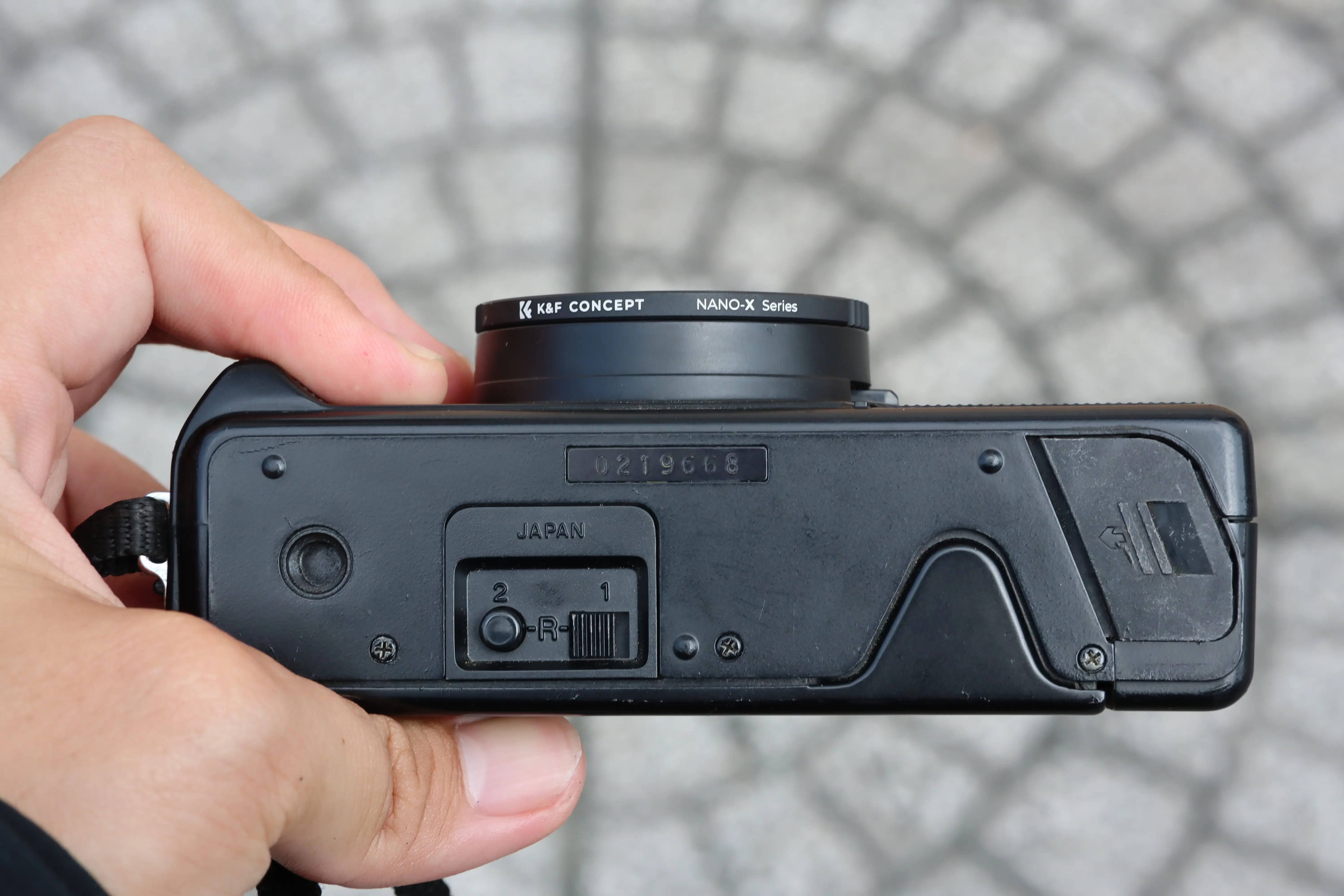 Góc nhìn từ dưới đáy máy ảnh film Nikon L35AF, hiển thị rõ nắp pin, lỗ gắn tripod và công tắc tua film (rewind switch) thủ công