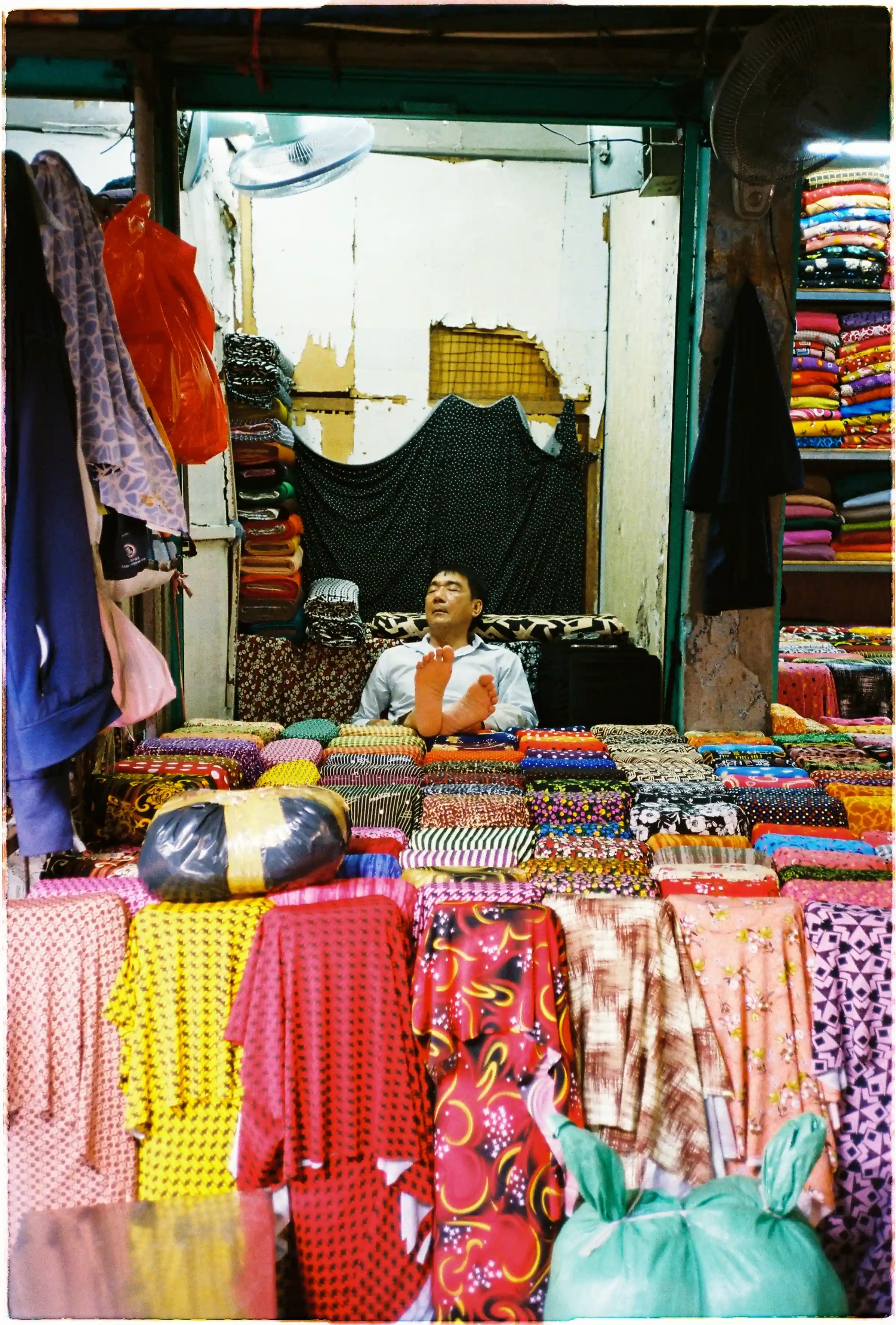 Ảnh chụp bằng Nikon L35AF trong sạp vải thiếu sáng, minh họa khả năng lấy nét chuẩn xác và sự hoạt động êm ái khi chụp người đang ngủ - Fuji 400.